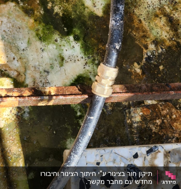 צינור שחור עם מחבר מתכת על רקע חלוד